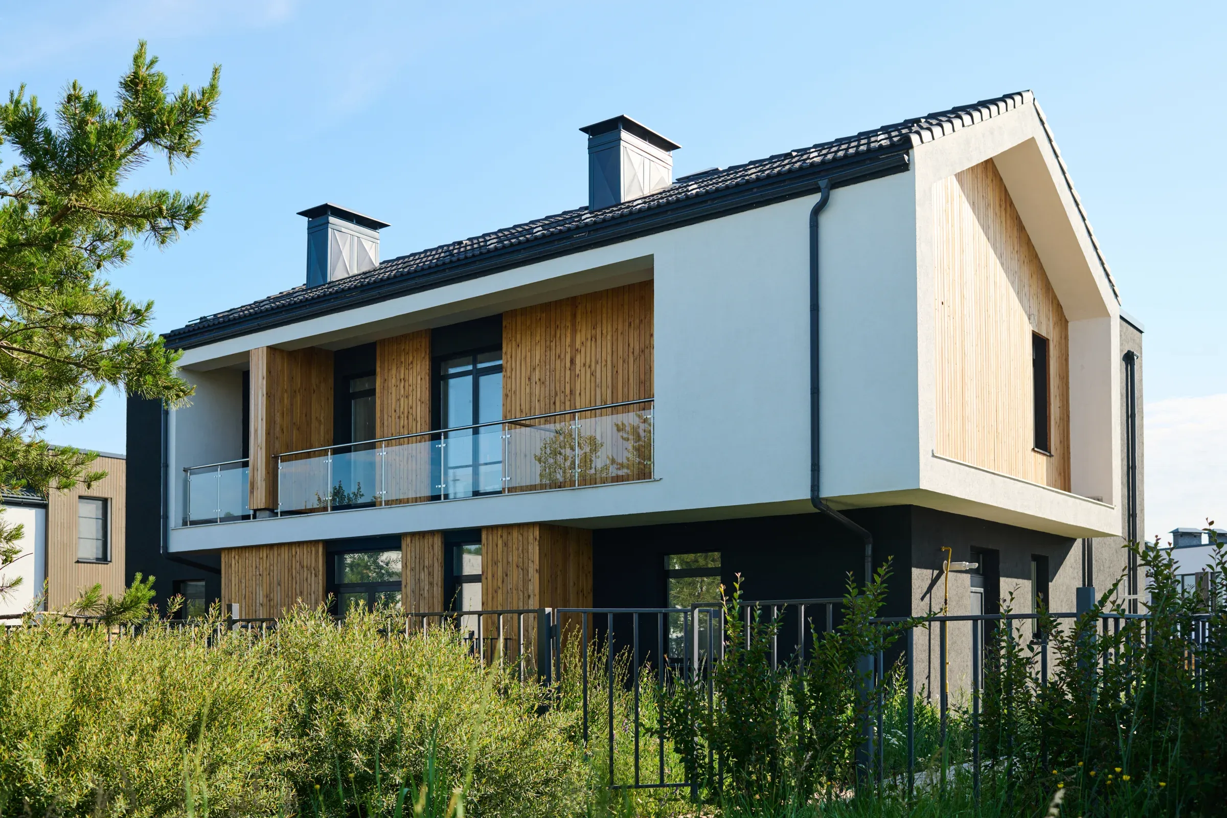Modernes Zweifamilienhaus mit Holzfassade, Satteldach und Garten bei Sonnenschein